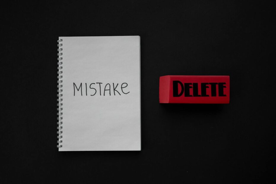A notebook with the word “MISTAKE” written on it next to a large red eraser labeled “DELETE,” placed on a black background.